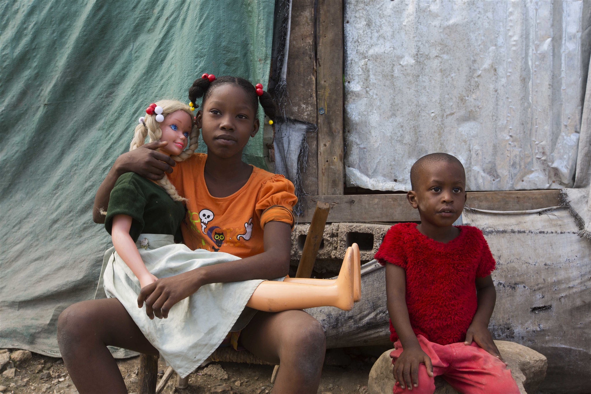 11-åriga Neissa kramar sin docka sittandes bredvid sin fyraåriga lillebror Olivier i ett läger i Port-au-Prince som sattes upp redan för sju år sedan efter jordbävningen i Haiti. I oktober drabbades det fattiga landet hårt igen i och med orkanen Matthew.