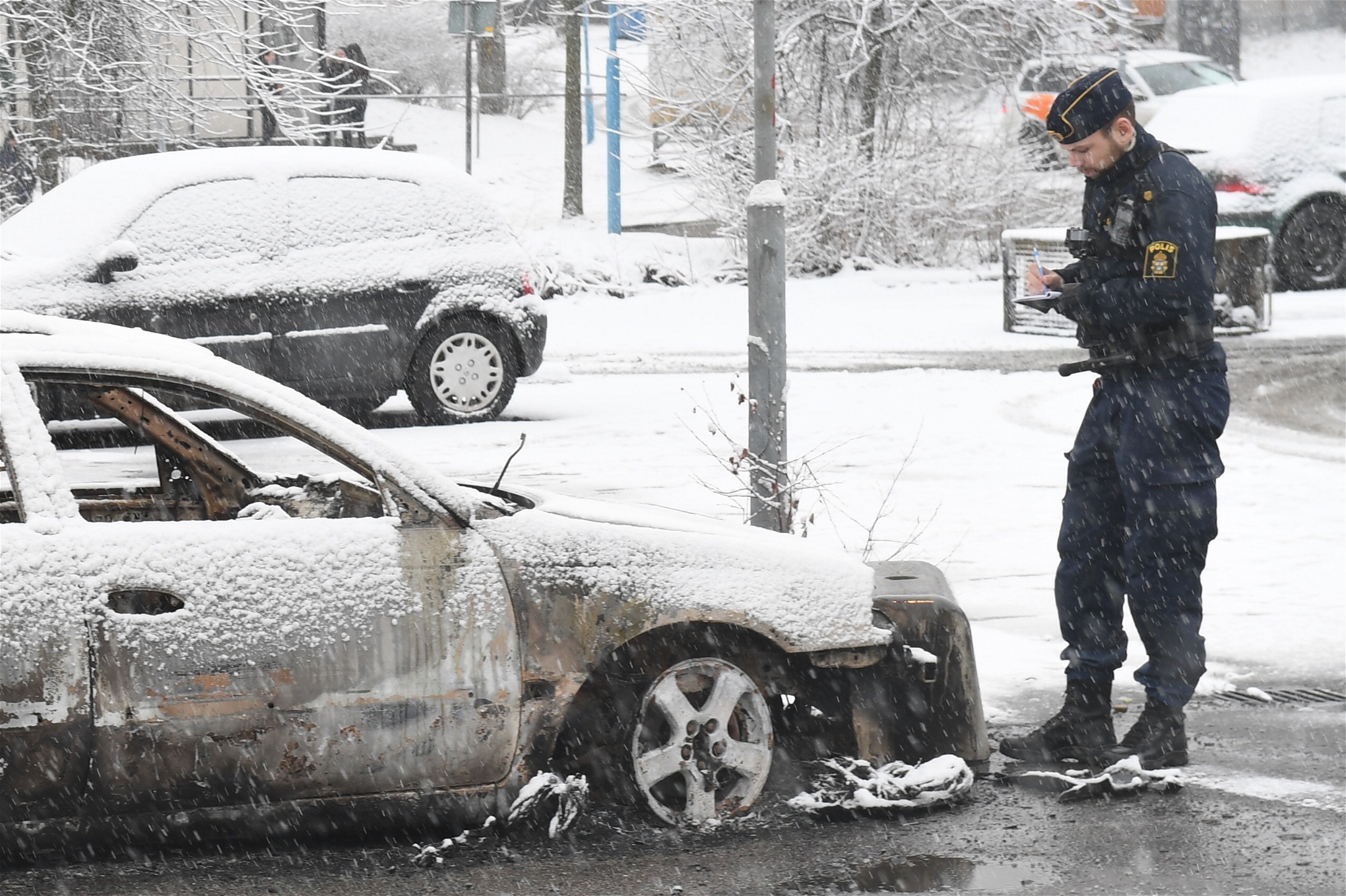 En polisman vid en utbränd bil på en parkering i förorten Rinkeby utanför Stockholm efter upploppet i februari i år. Oroligheterna började i samband med att polisen skulle göra ett ingripande och frihetsberöva en person. 