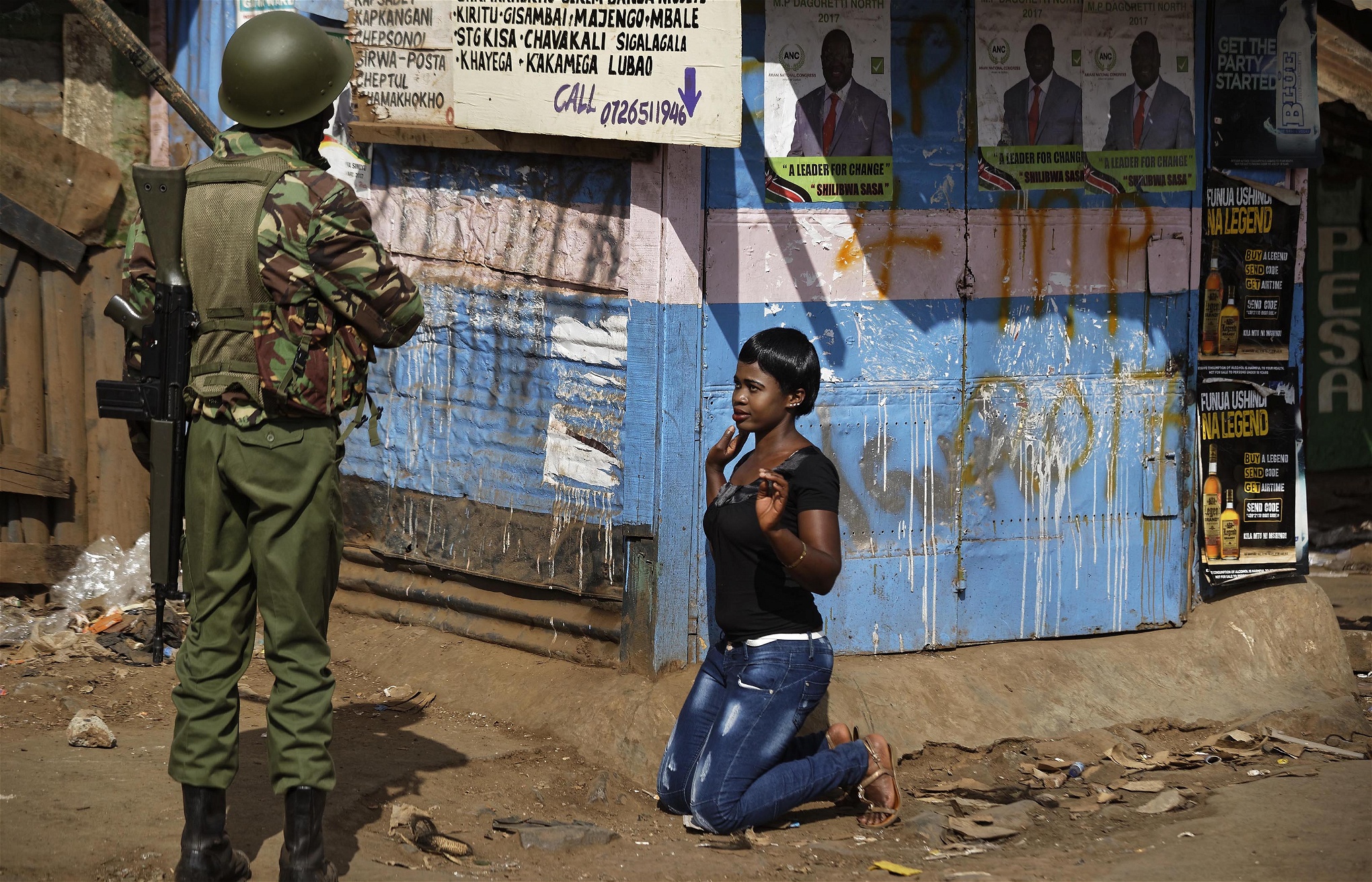 En kravallpolis tvingar ned en kvinna som han anklagar för att delta i upploppen på knä i Kawangware i Nairobi.