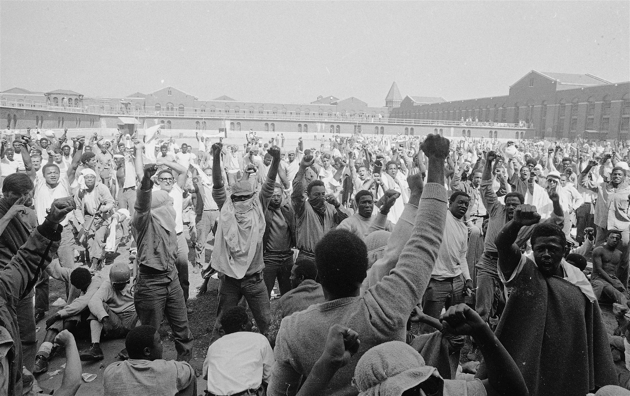 Fångar på Attica-fängelset under upproret 1971 lyfter sina knutna händer mot himlen.