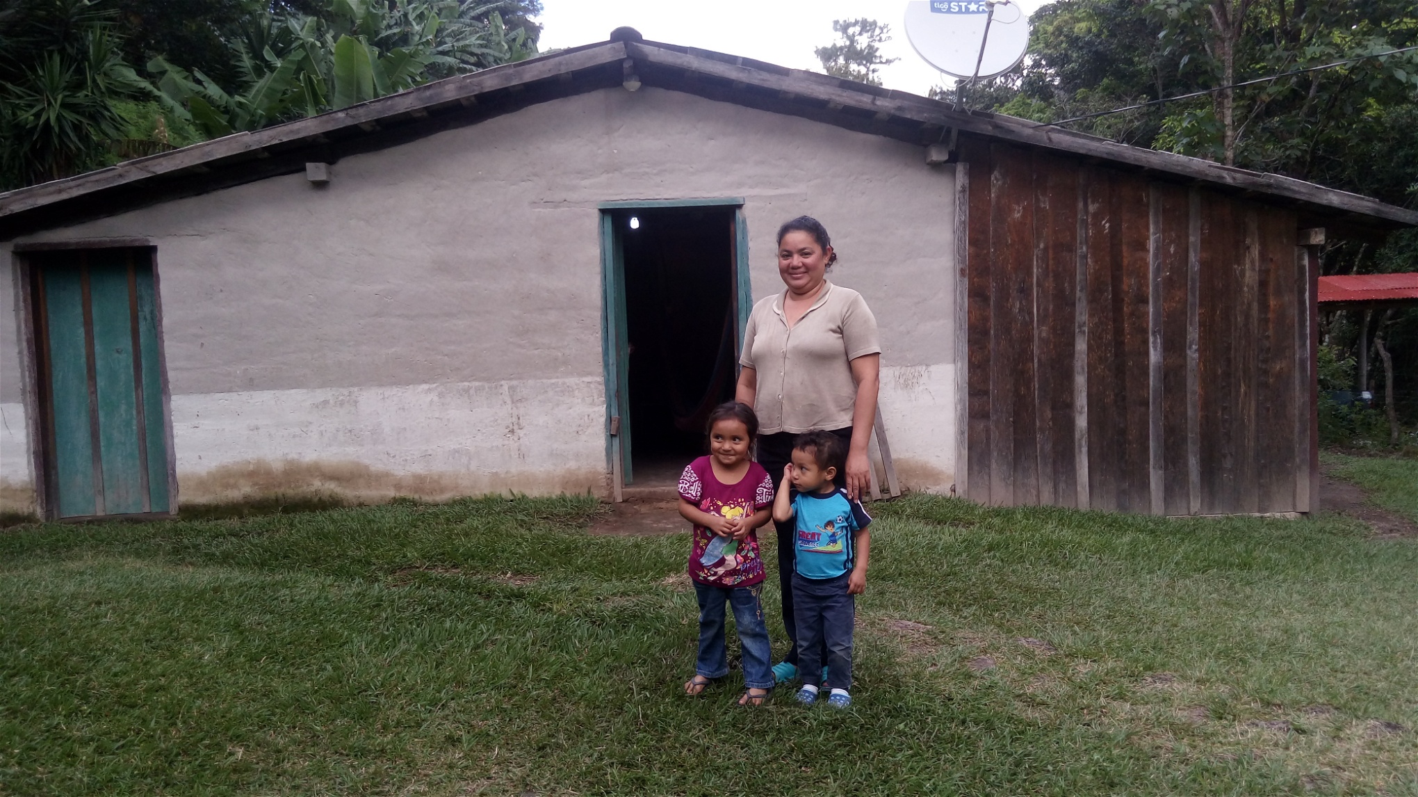 Läraren Carolina Martinez står tillsammans med sina barn utanför sitt hus i byn, där en lampa står tänd. Sedan 2012 har de 40 familjerna i Joya de Talchiga haft tillgång till el tack vare sitt eget engagemang. 