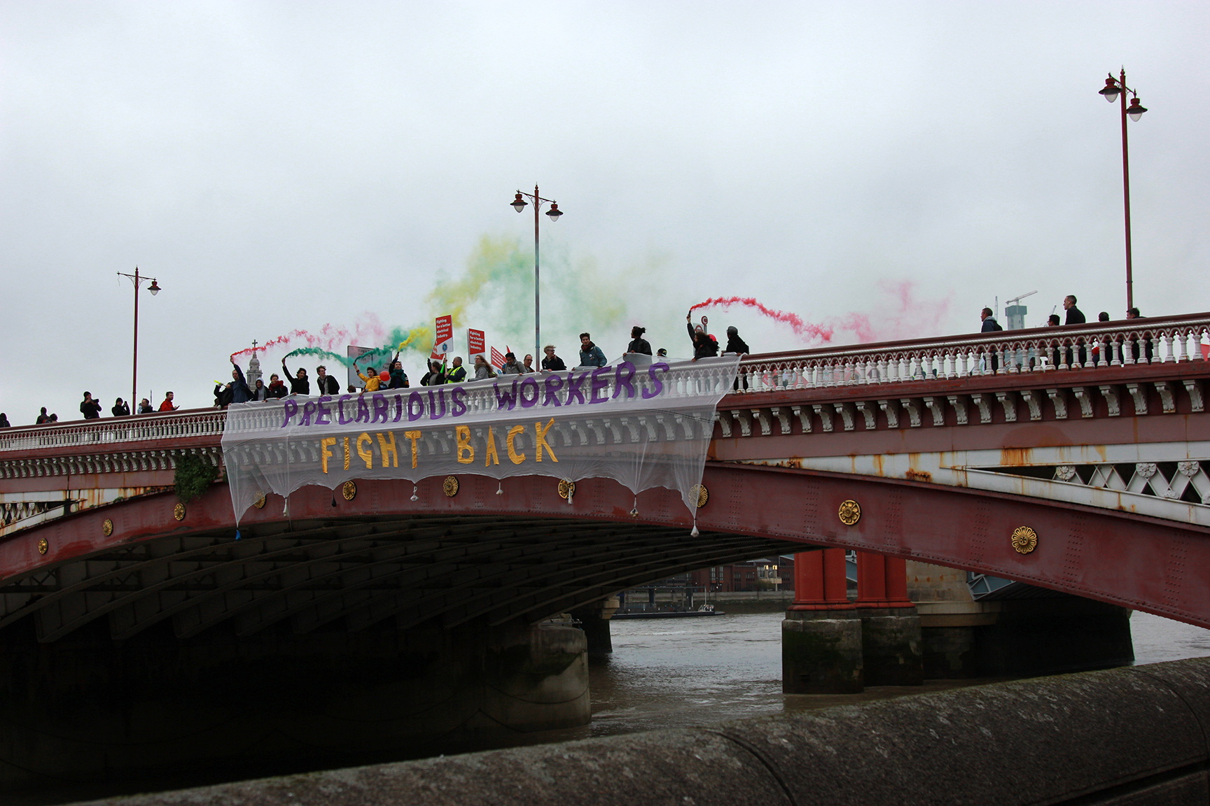 Demonstranterna hissar ned en banderoll vid Blackfriarsbron. Fackförbundet IWGB beskriver manifestationen som ”den största prekära demonstrationen i landet någonsin”.