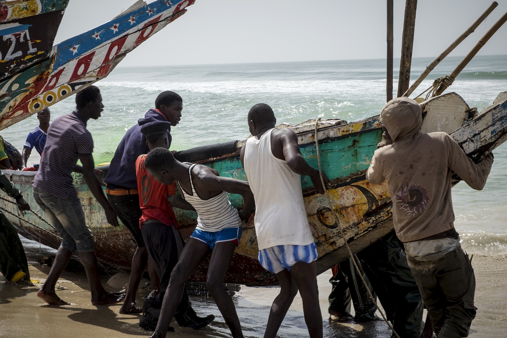 Några fiskare kämpar för att få upp sin fiskebåt på land. I Senegal har fisket alltid varit den största industrin.