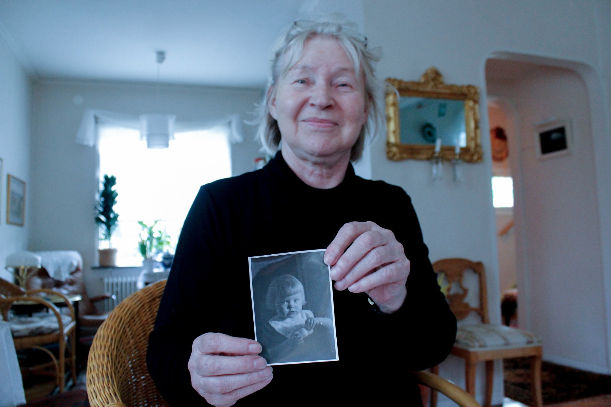 Kirsti Sjöström håller upp ett fotografi föreställande henne själv vid fyra års ålder. Fotot är taget samma år som familjen tvingades på flykt.