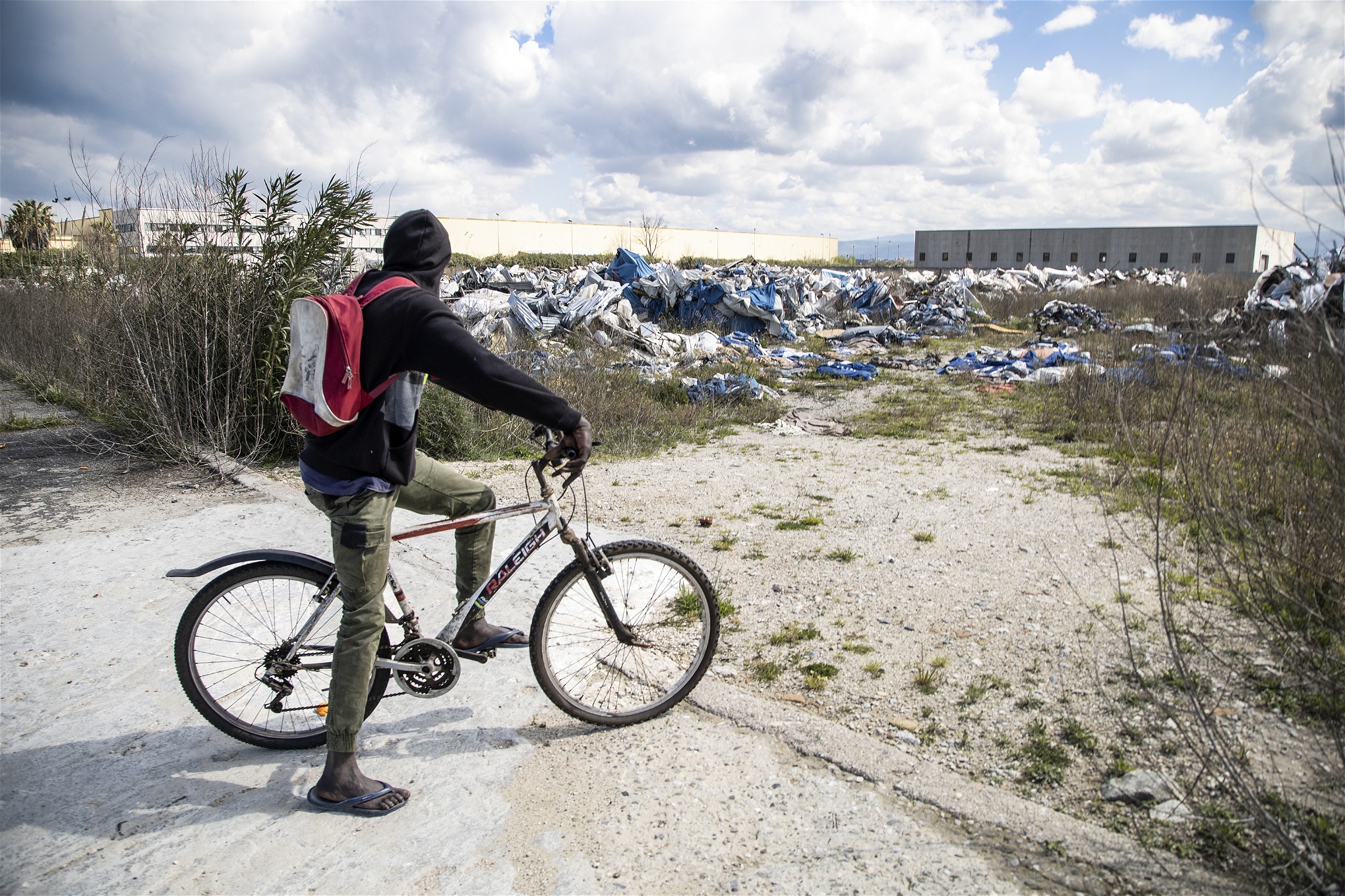 Foto: Valerio NicolosiEn migrantarbetare på cykel blickar ut över den rivna tältstaden.
