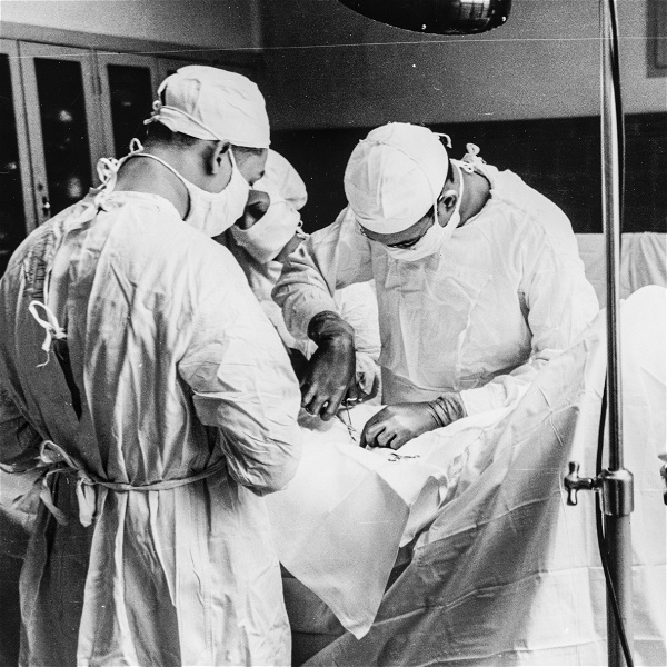 Svartvitt fotografi där tre operationspersonal står runt en patient täckt av vita lakan. En kirurg använder en kirurgsax i patientens öppna snitt. Bilden är från 1941.