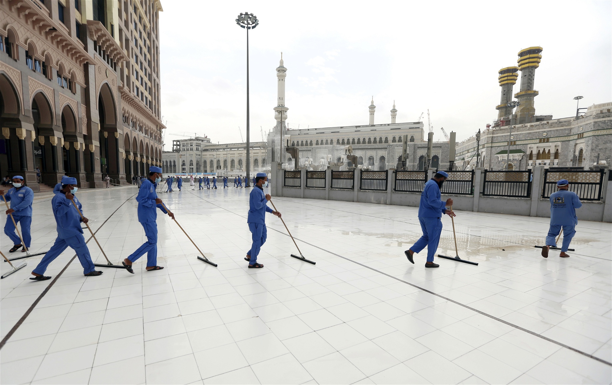 Städare i blåa skyddskläder svabbar golvet utanför en moské.