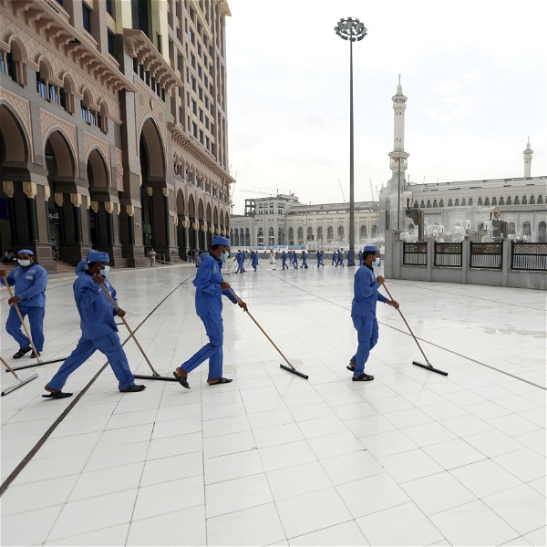 Städare i blåa skyddskläder svabbar golvet utanför en moské.