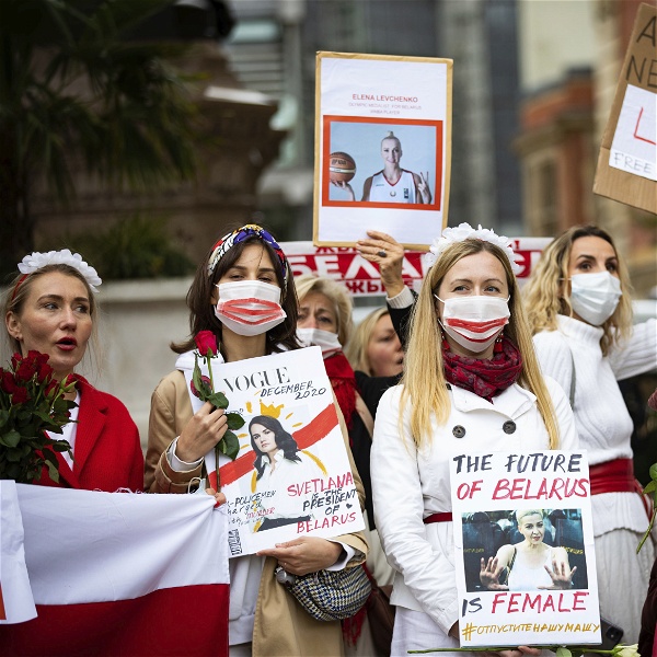 Kvinnor med vita kläder, håller rödvita flaggor, rosor och plakat där det bland annat står The future of Belarus is female.