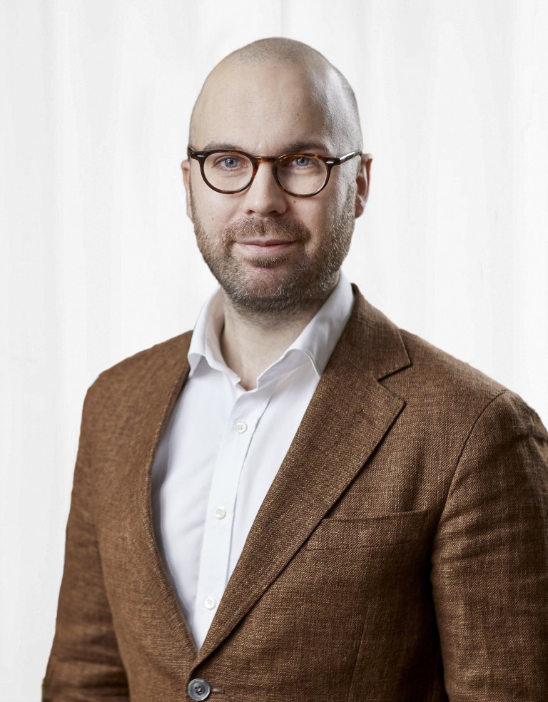 Porträttbild på Jonathan Öhman i brun kavaj och vit skjorta. 
