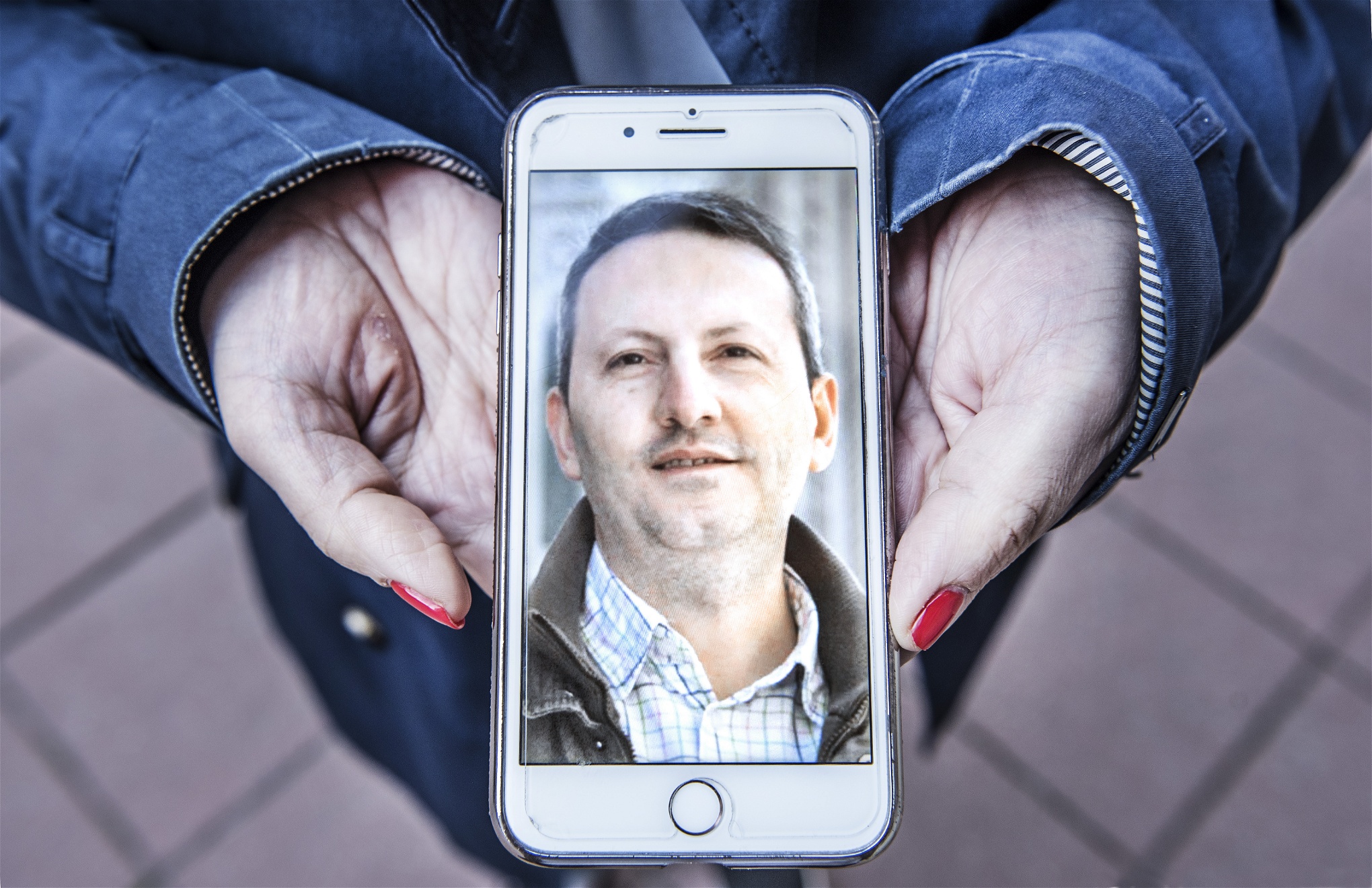 Två händer håller fram en mobiltelefon som visar ett porträtt av Ahmadreza Djalali.