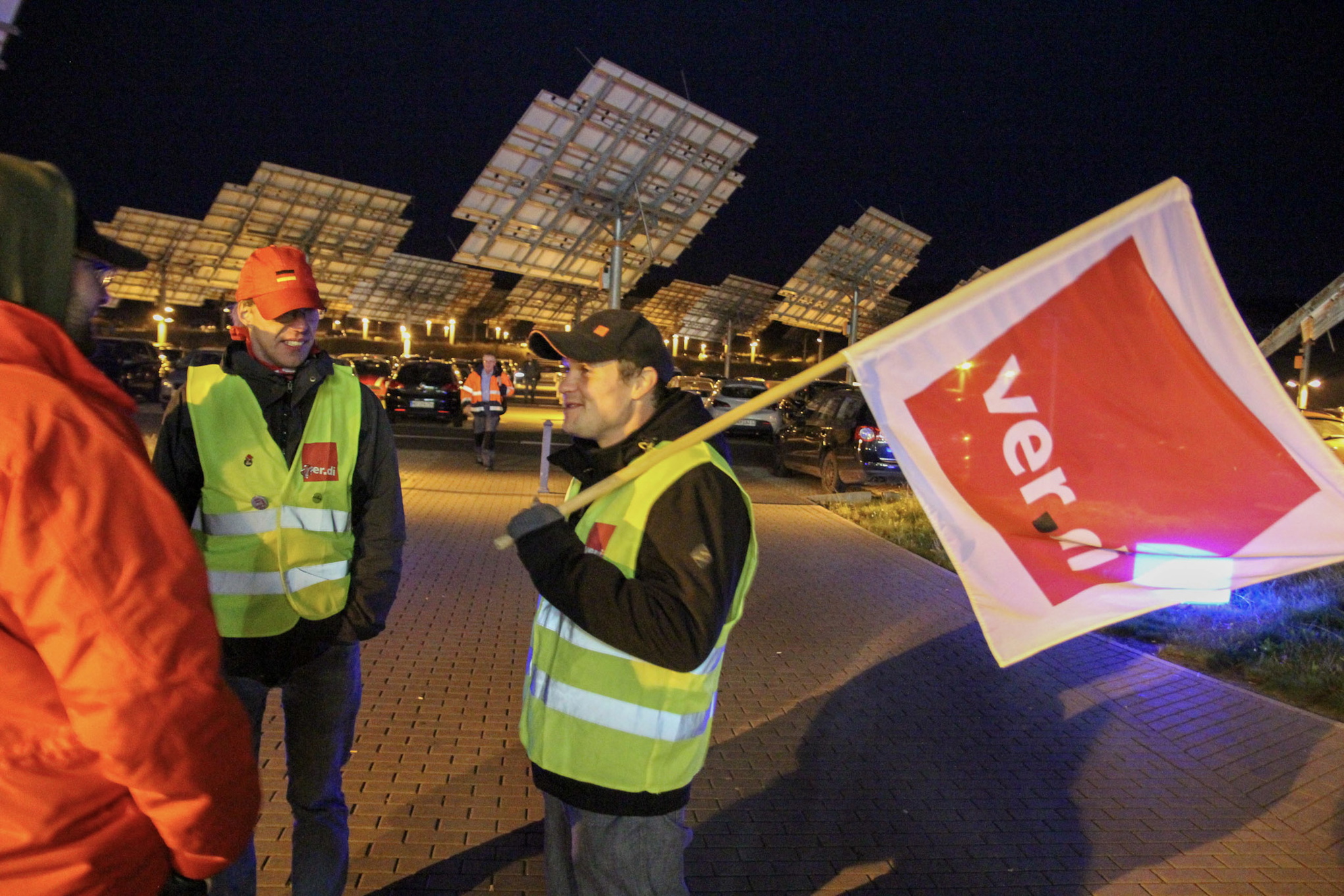 Christian Krähling och en kamrat i reflexvästar. Christian har en röd och vit flagga med texter Verdi över axeln. Det är mörkt ute. 