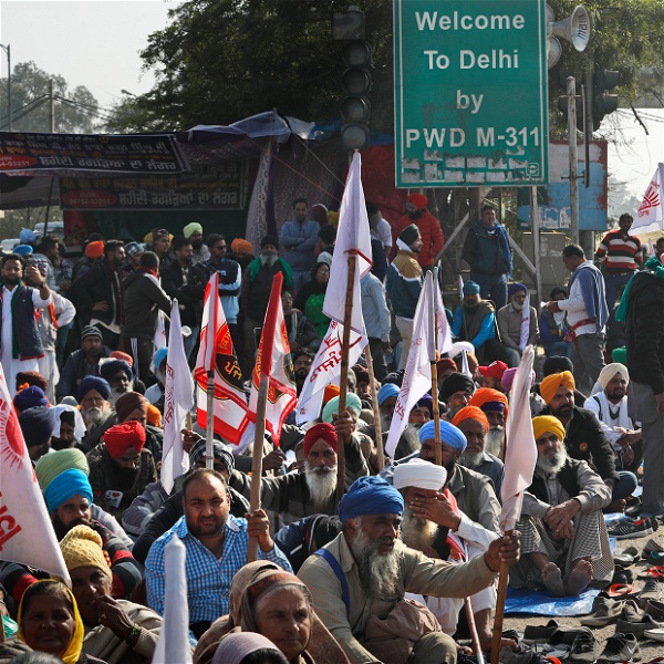 Indiska bönder sitter på marken framför en skylt med texten "Välkommen till Delhi"
