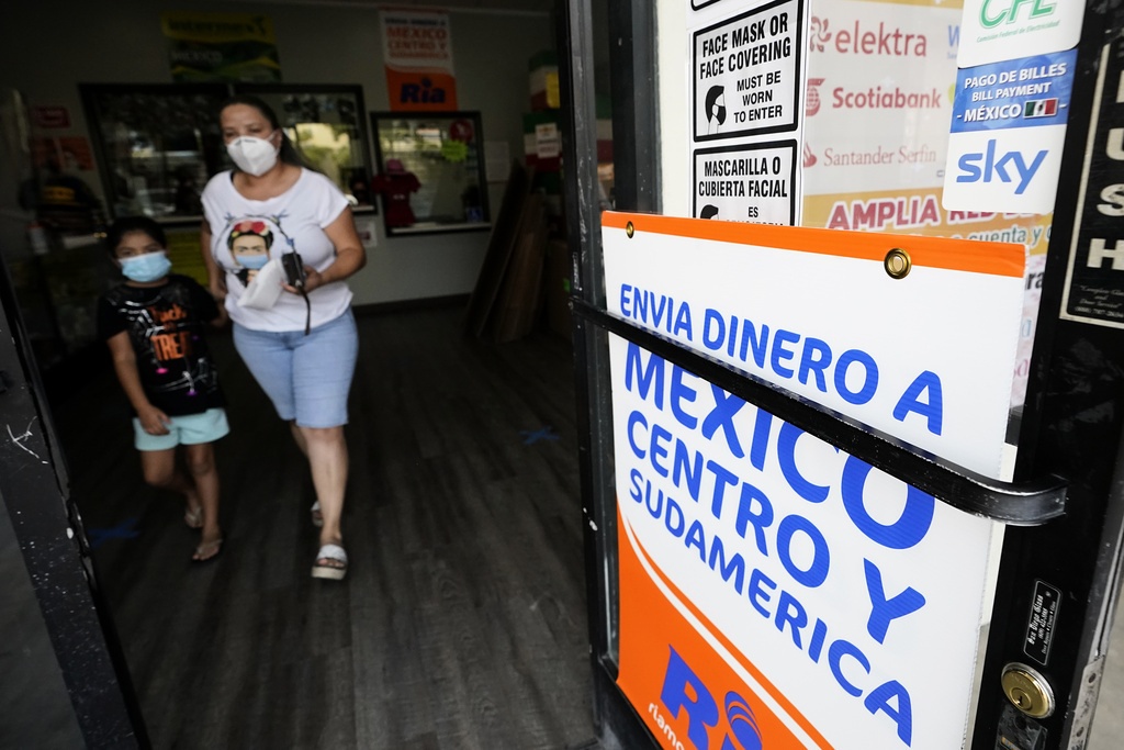 En kvinna och ett barn, båda med munskydd, lämnar en butik. På en skylt står det på spanska att man här kan skicka pengar till Central- och Sydamerika.