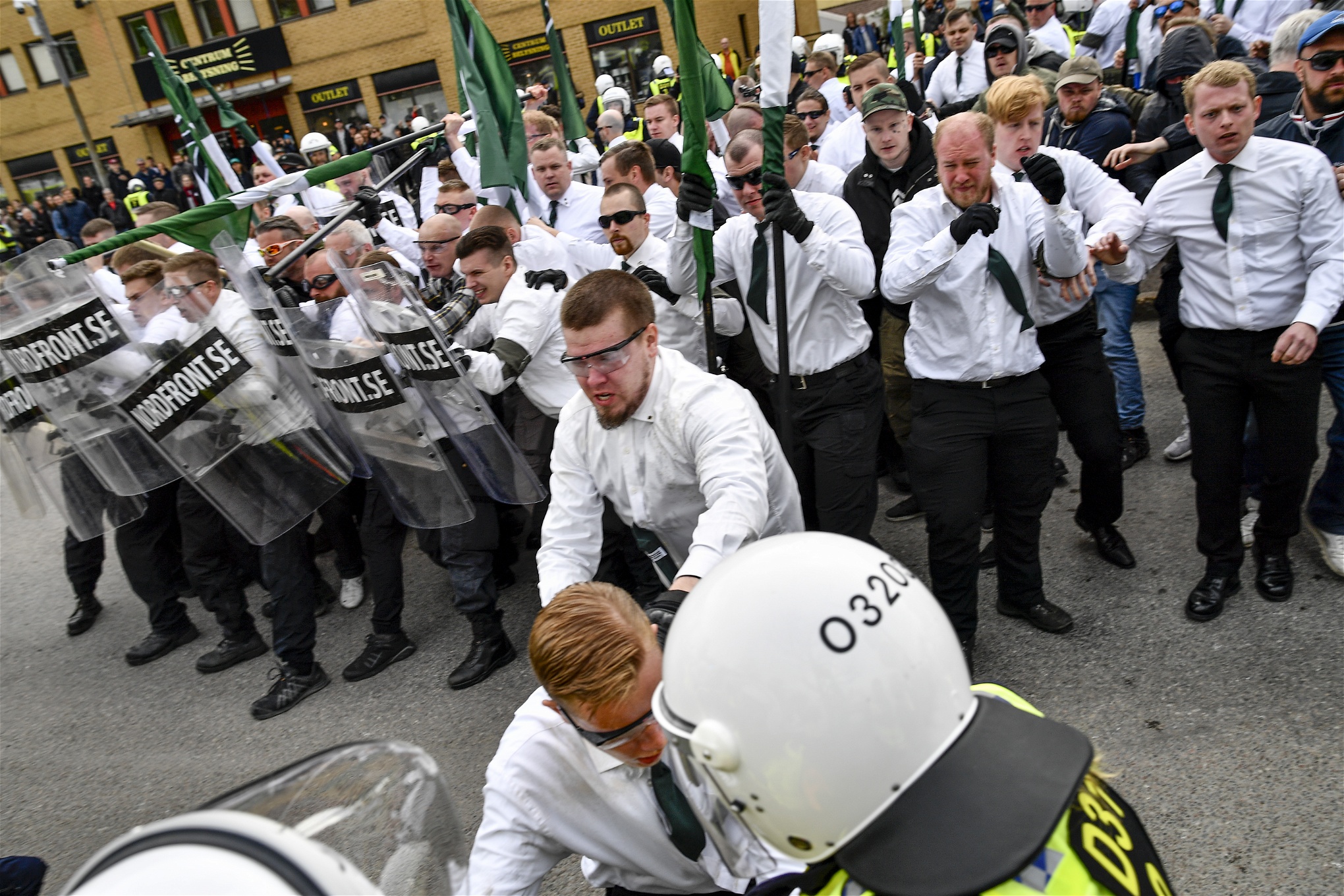 Nazistiska organisationen Nordiska motståndsrörelsen (NMR) demonstration i Kungälv på första maj 2019. De är klädda i vita skjortor och gröna slipsar och har gröna flaggor och plexiglas-sköldar.