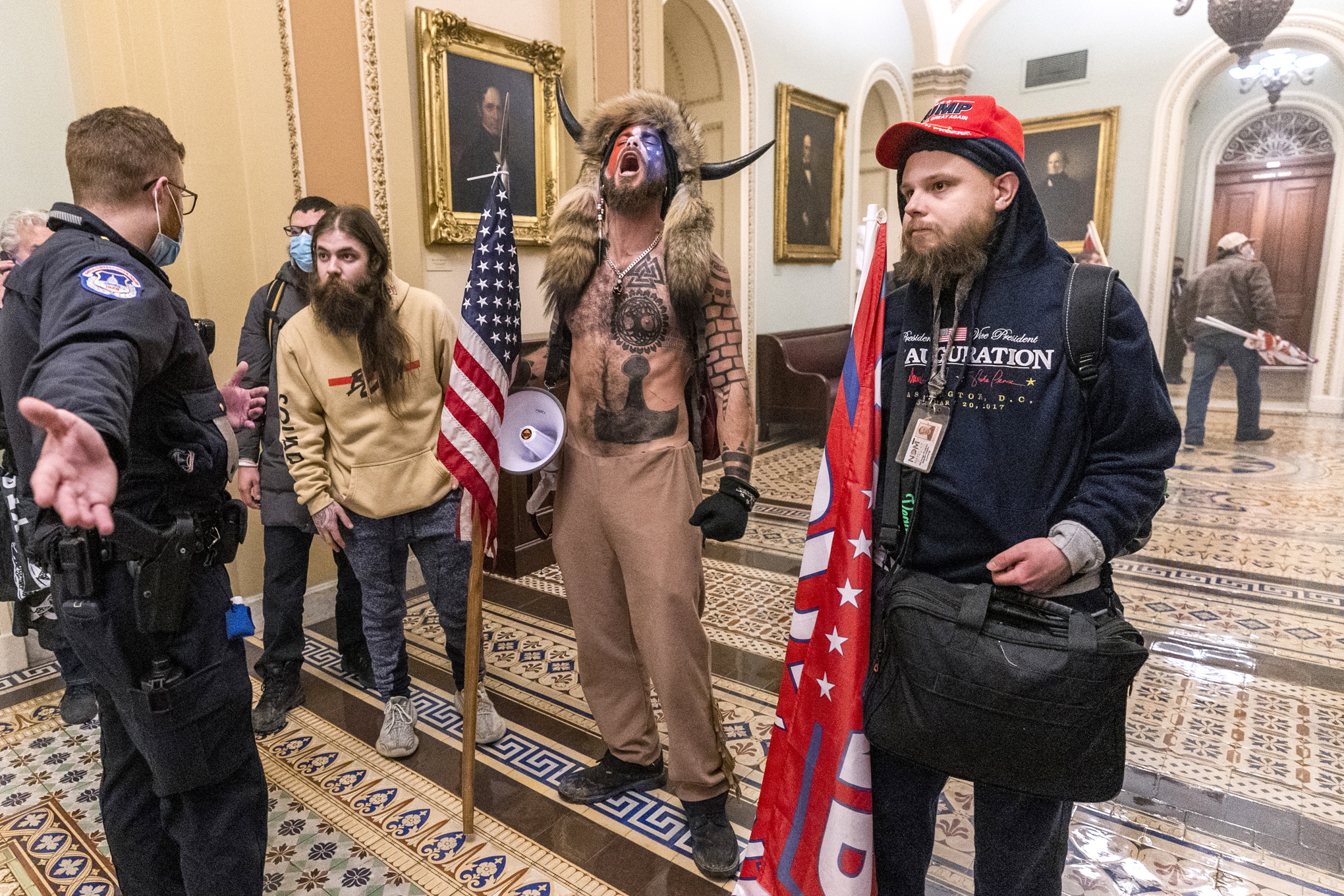 Fyra Trumpsupportrar utanför senatskammaren, inne i Kapitoleum. En av dem har buffelhorn på huvudet, päls över axlarna och många tatueringar.