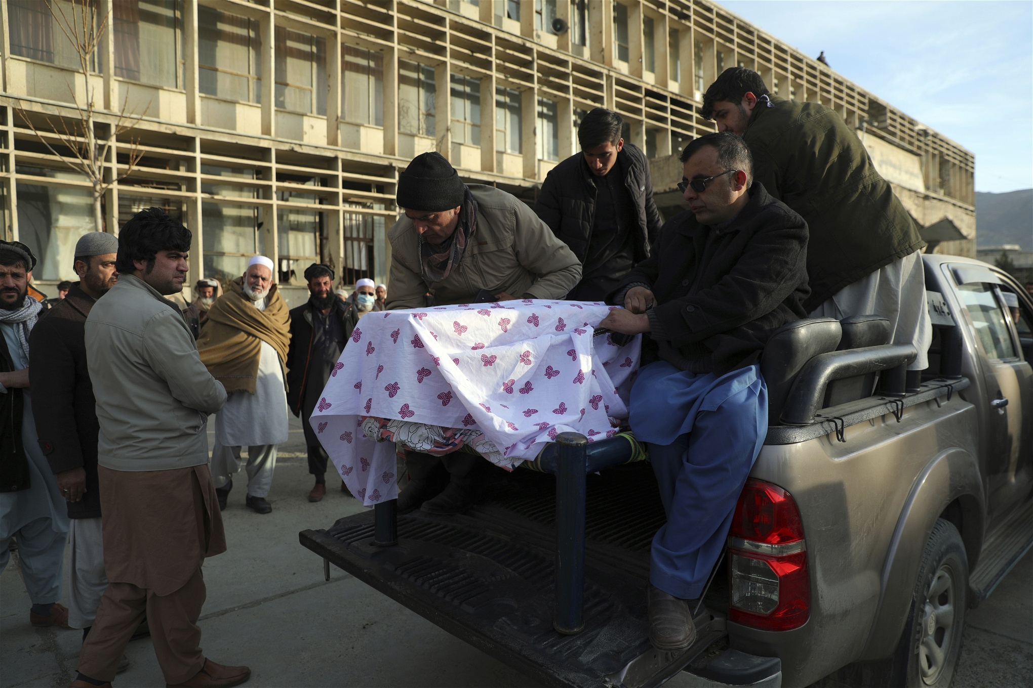 Fyra män lyfter av en kista täckt av ett vitt tyg, från flaket av en bil.