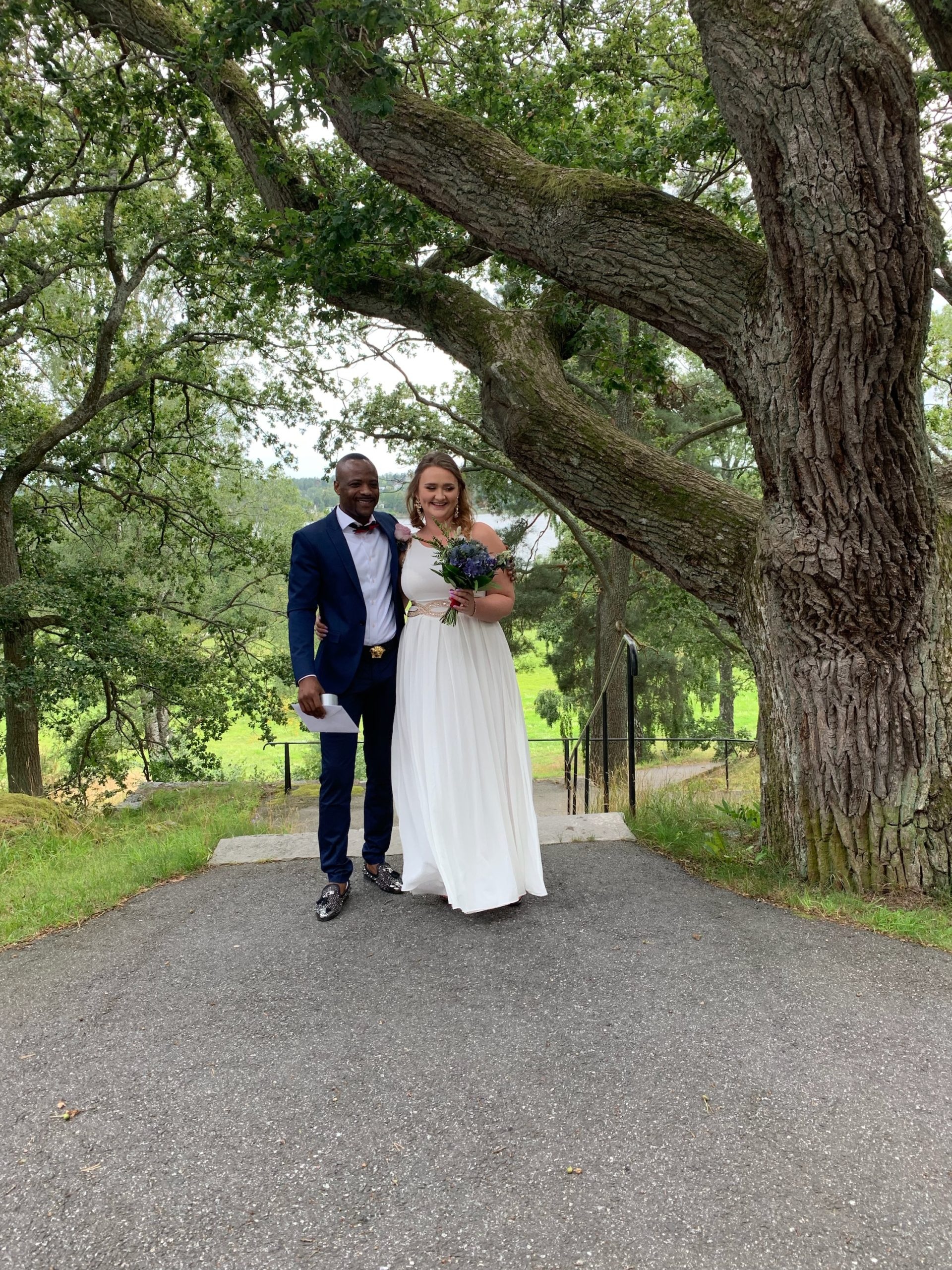 David och Johanna klädda för bröllop bredvid ett stort grönskande träd.