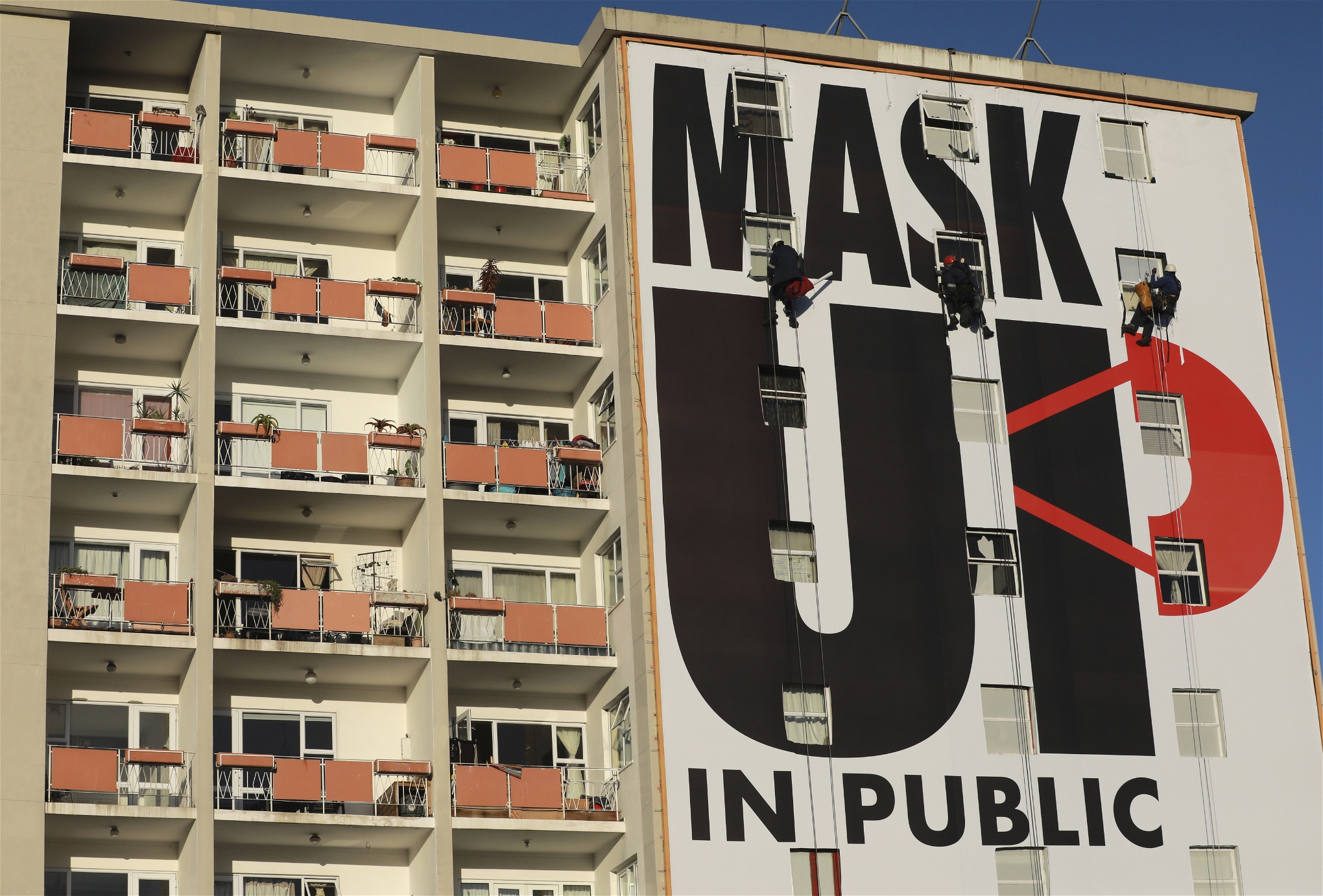 En reklamtavla som täcker en husfasad. Texten lyder Mask up in public.