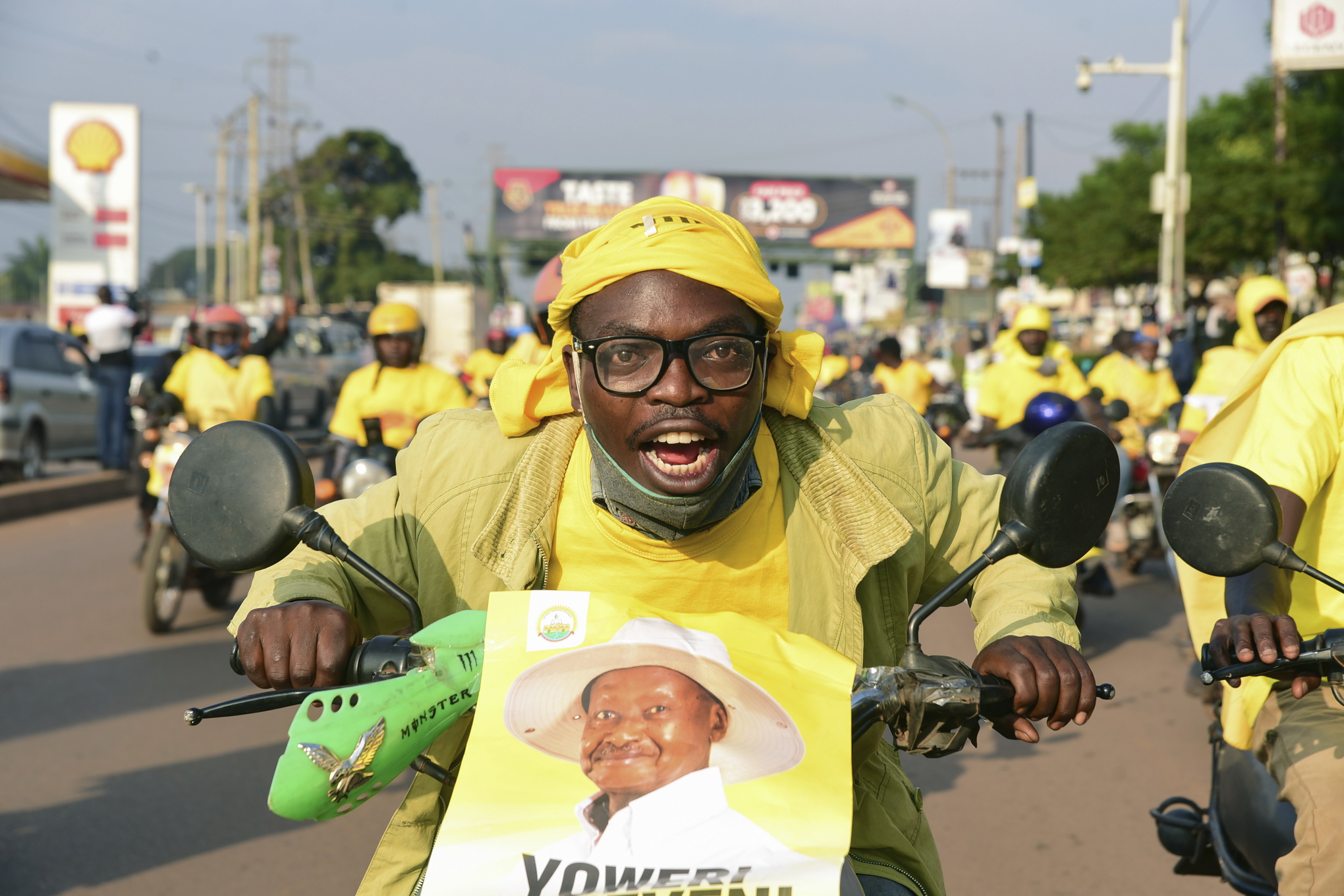 En gulklädd supporter av president Museveni åker moped med en bild på Museveni framtill. 