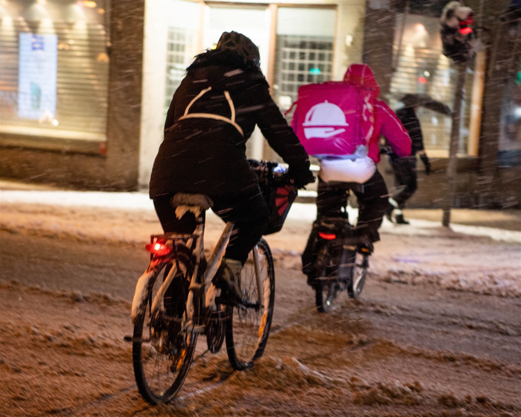 Foodoracyklist cyklar bort från kameran på en snömoddig gata.