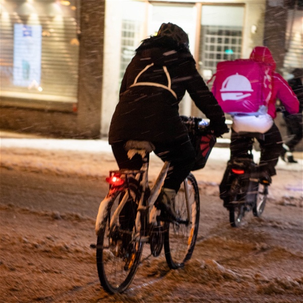 Foodoracyklist cyklar bort från kameran på en snömoddig gata.