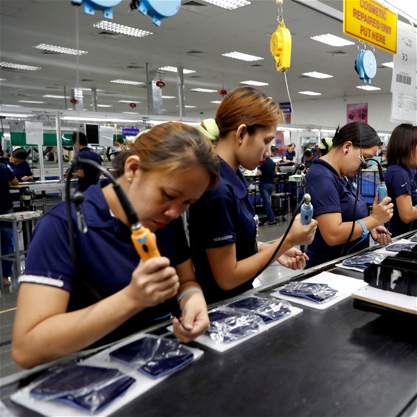 Kvinnor i blåa kläder arbetar med elektroniktillverkning.