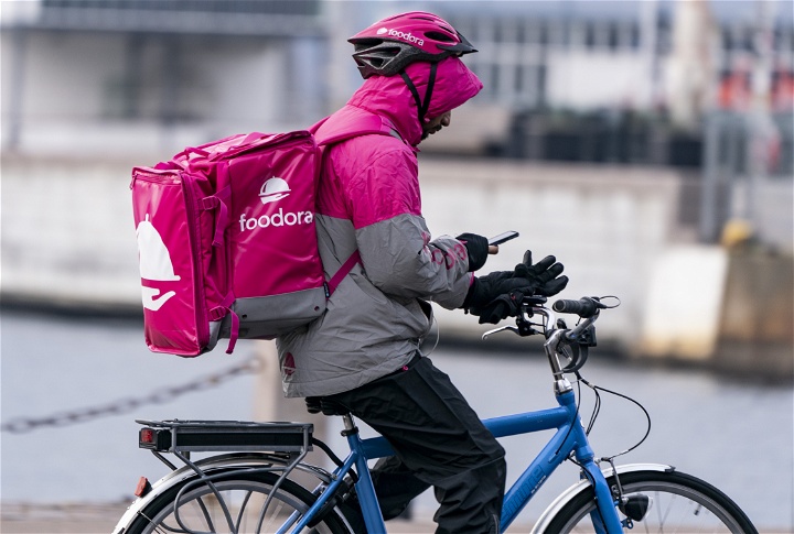 Foodora-cyklist med rosa ryggsäck cyklar och kollar på sin mobiltelefon.
