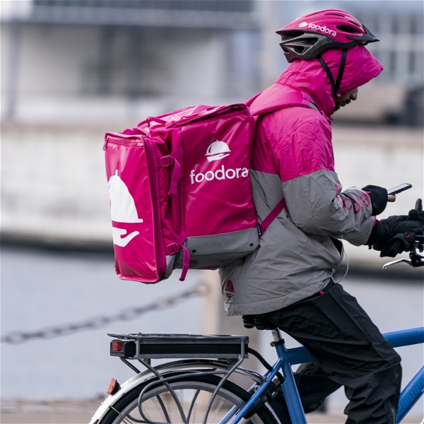 Foodora-cyklist med rosa ryggsäck cyklar och kollar på sin mobiltelefon.