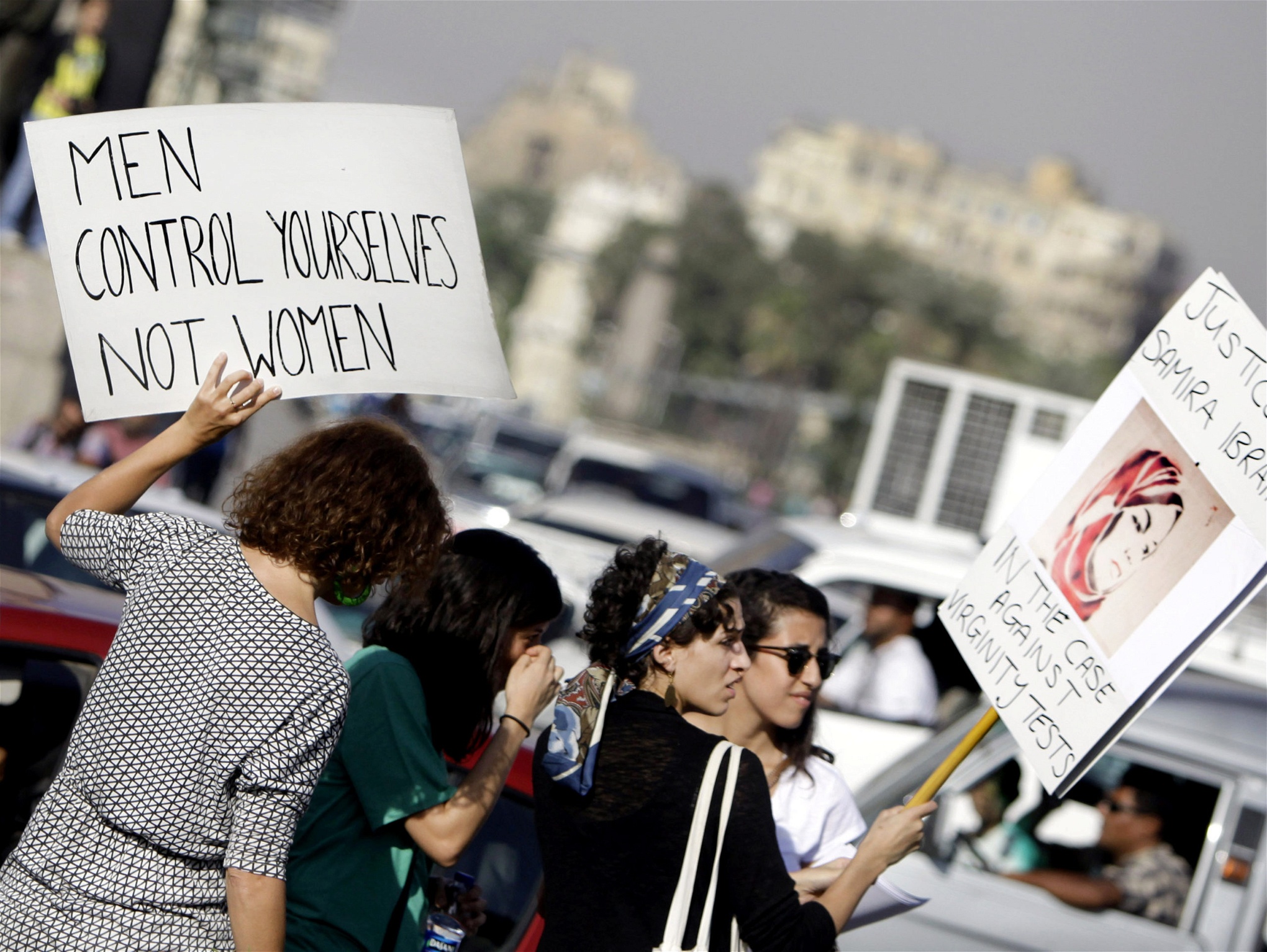 Kvinnor på en trafikerad gata håller upp plakat. Ett av dem har texten, Men control yourselves, not women. 