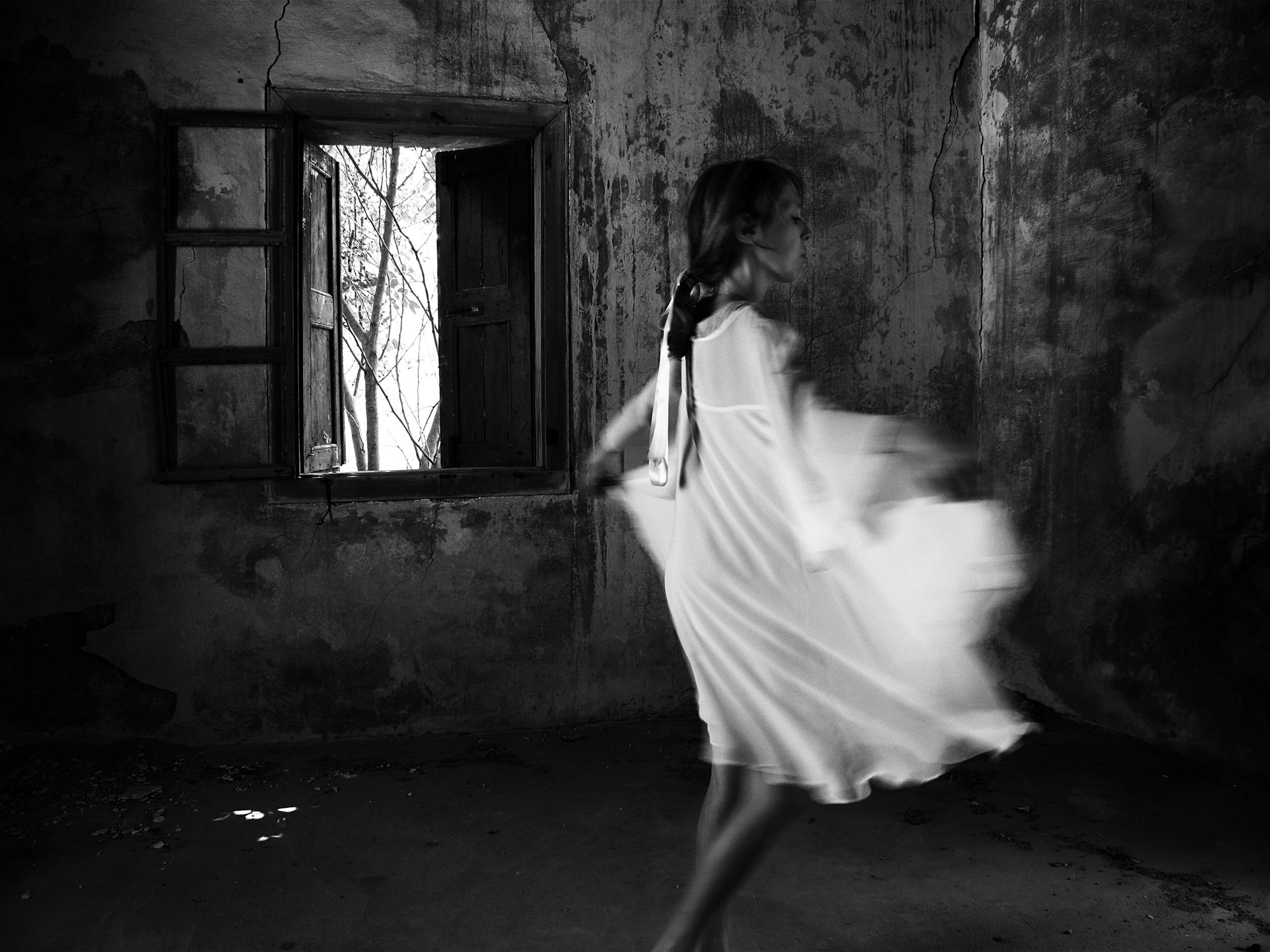 Svartvit bild där Lene Marie Fossen syns dansandes i ett avskalat rum i vit klänning.