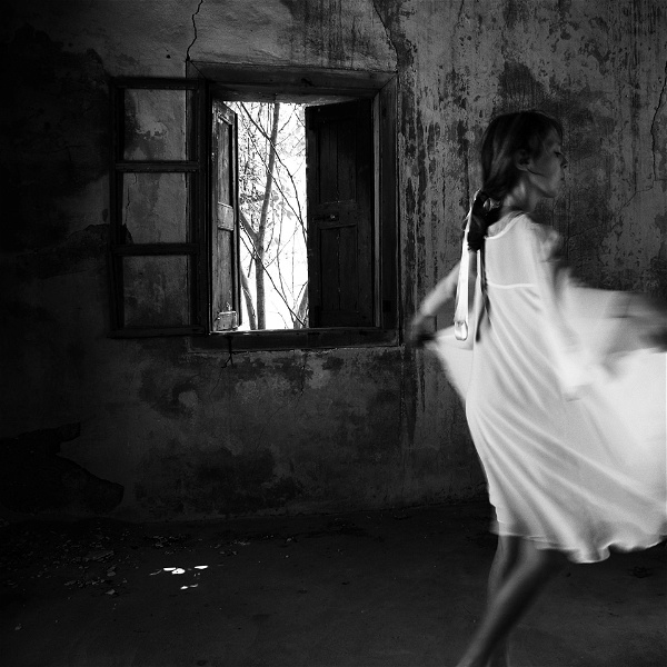 Svartvit bild där Lene Marie Fossen syns dansandes i ett avskalat rum i vit klänning.