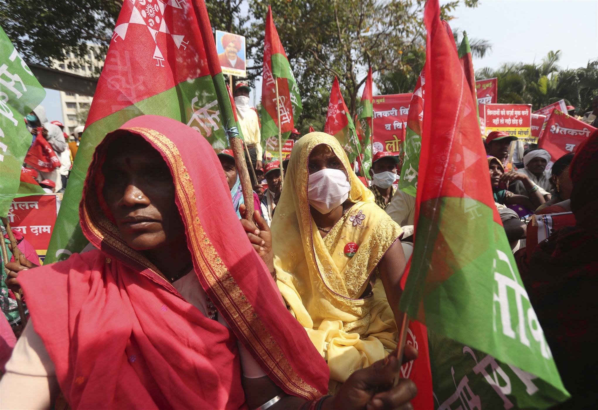 Indiska kvinnliga bönder i röda och gula saris och med röda och gröna flaggor demonstrerar.