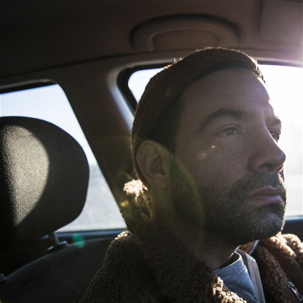 Pierro Dall’Osso fotograferad bakom ratten i sin bil, från passagerarsätet. Solen lyser in i sidorutan.