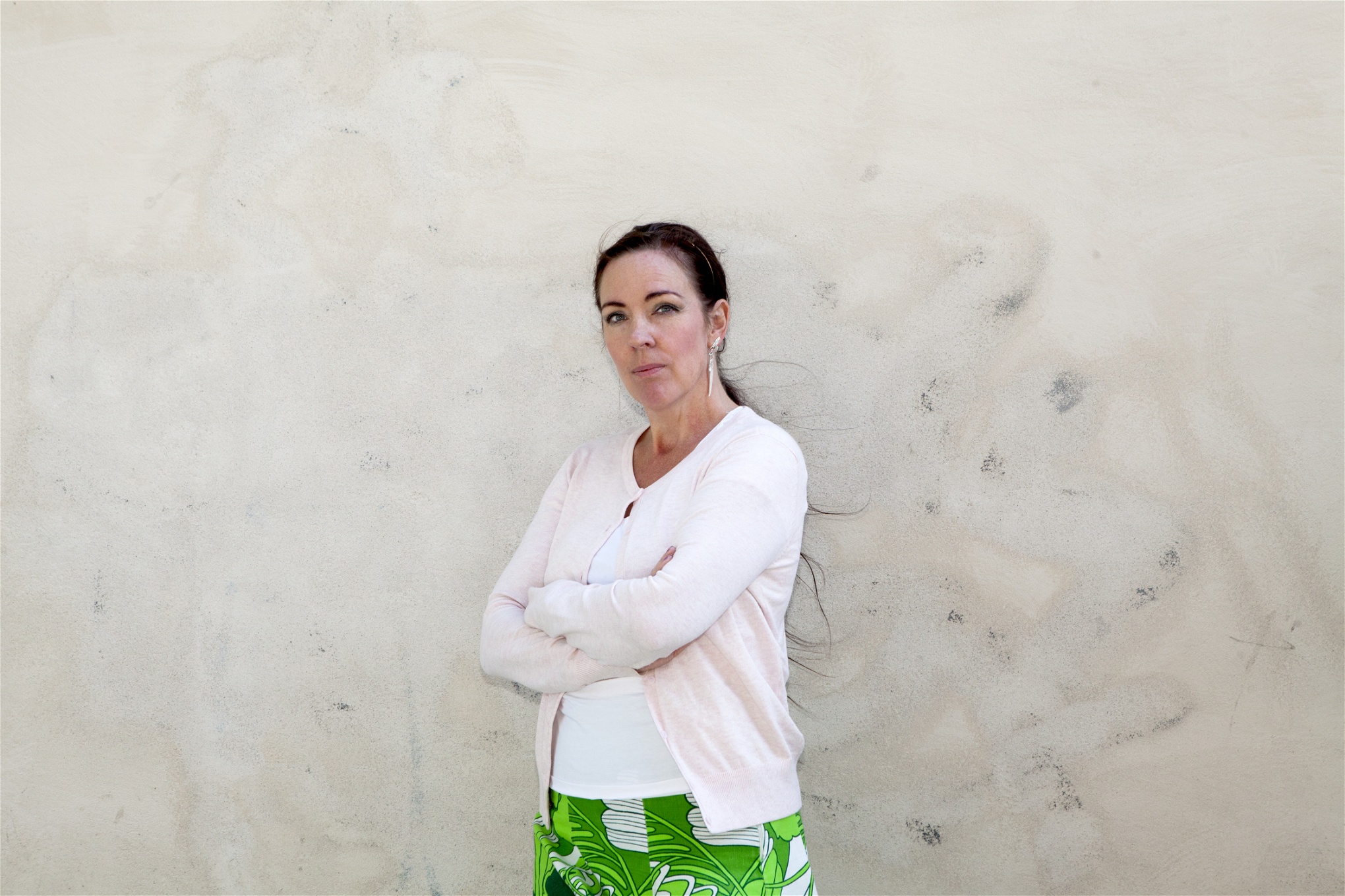 Jenny Westerstrand i vit kofta och grönmönstrad kjol framför en ljus vägg. 