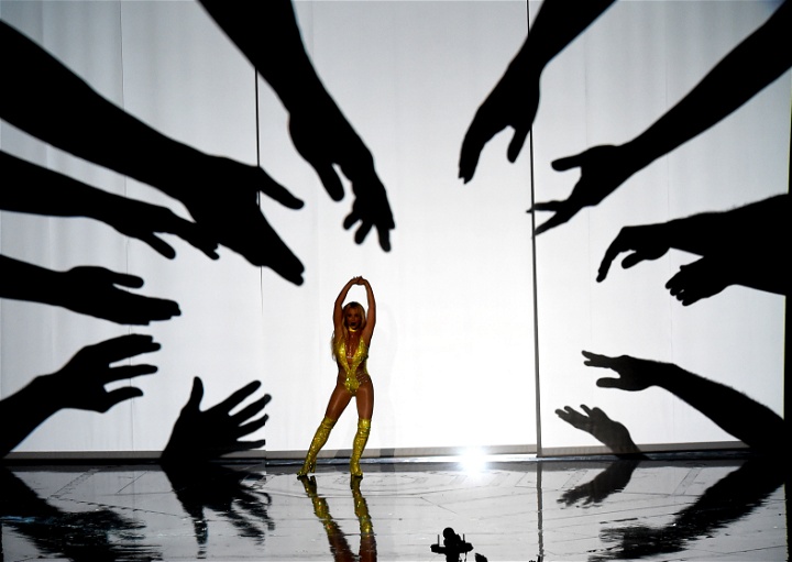 Britney Spears på en scen med stora siluetter av händer som sträcker sig mot henne.