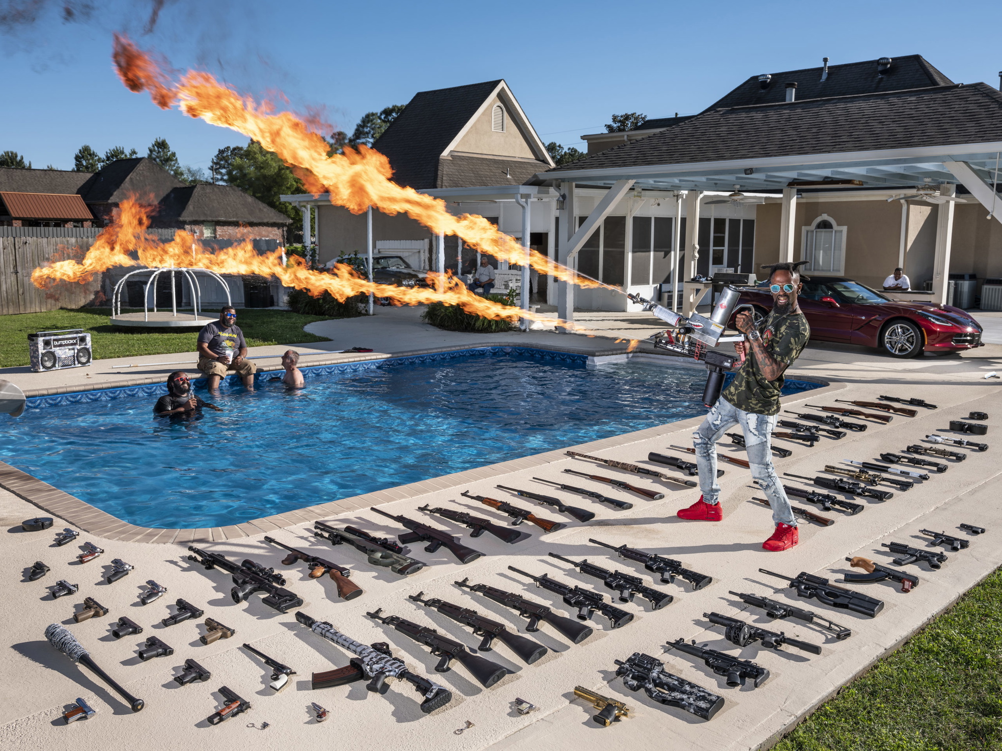 En man avfyrar ett eldvapen framför en pool. På marken ligger mängder av automatvapen uppradade.