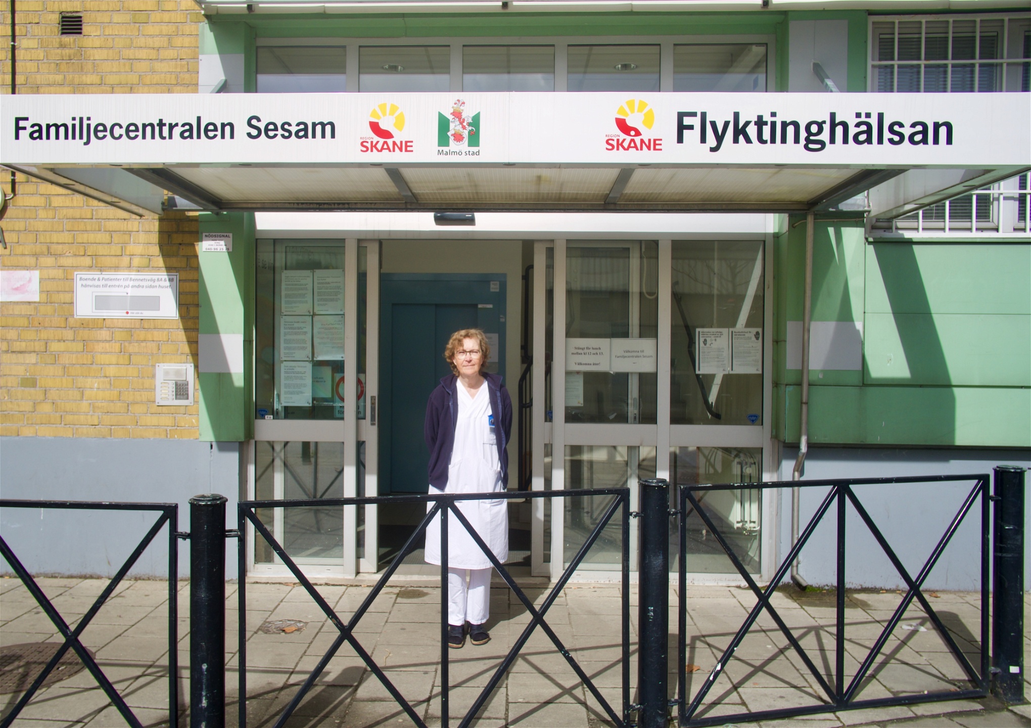 Åsa Wieslander, sjuksköterska på Flyktinghälsan, i vita arbetskläder framför Flyktinghälsans entré.