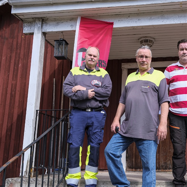 Göran Israelsson, Patrik Aronsson och Anders Pettersson utanför Pappersavdelningens rödmålade hus på Kvarnsvedens pappersbruk. De står på trappan. Bakom dem hänger två vimplar med Pappers logga på.