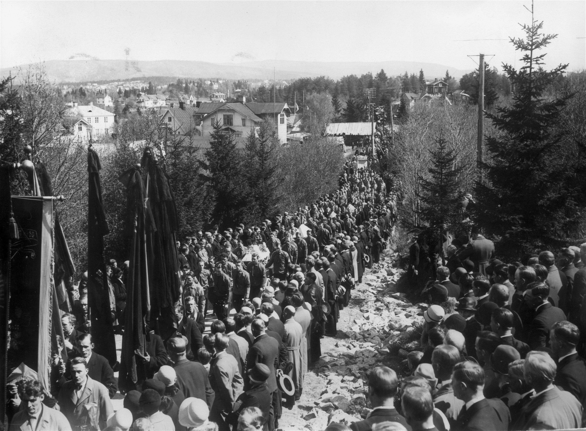 Begravningsföljet efter skotten i Ådalen sträcker sig längs en grankantad väg där många åskådare finns vid vägkanten.