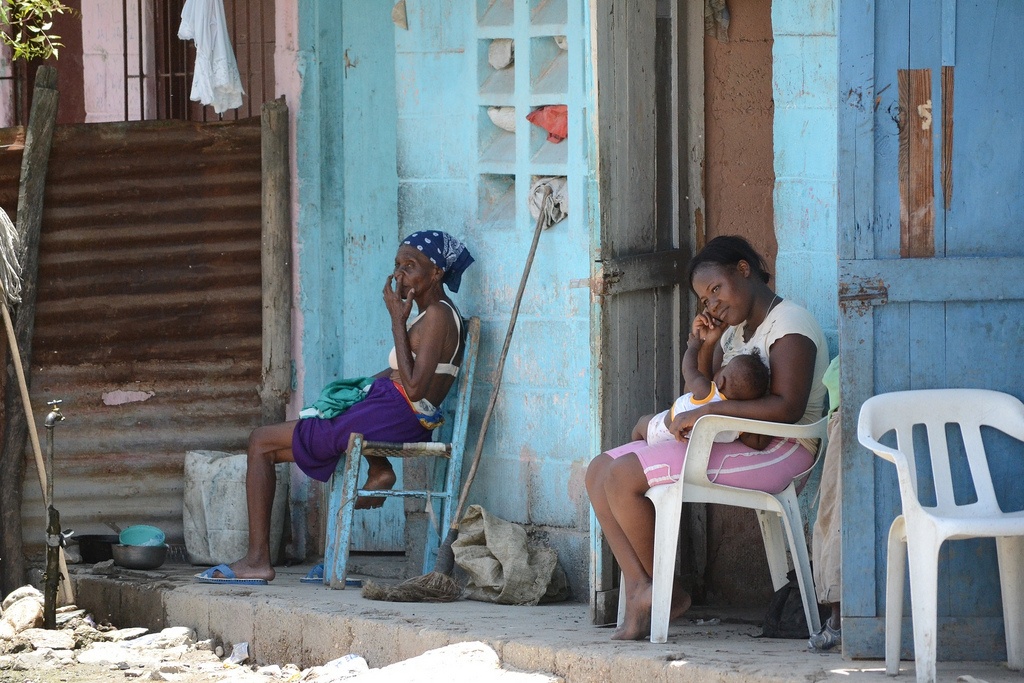 Två kvinnor sitter utanför ett bostadshus, den ena med ett litet barn i famnen.