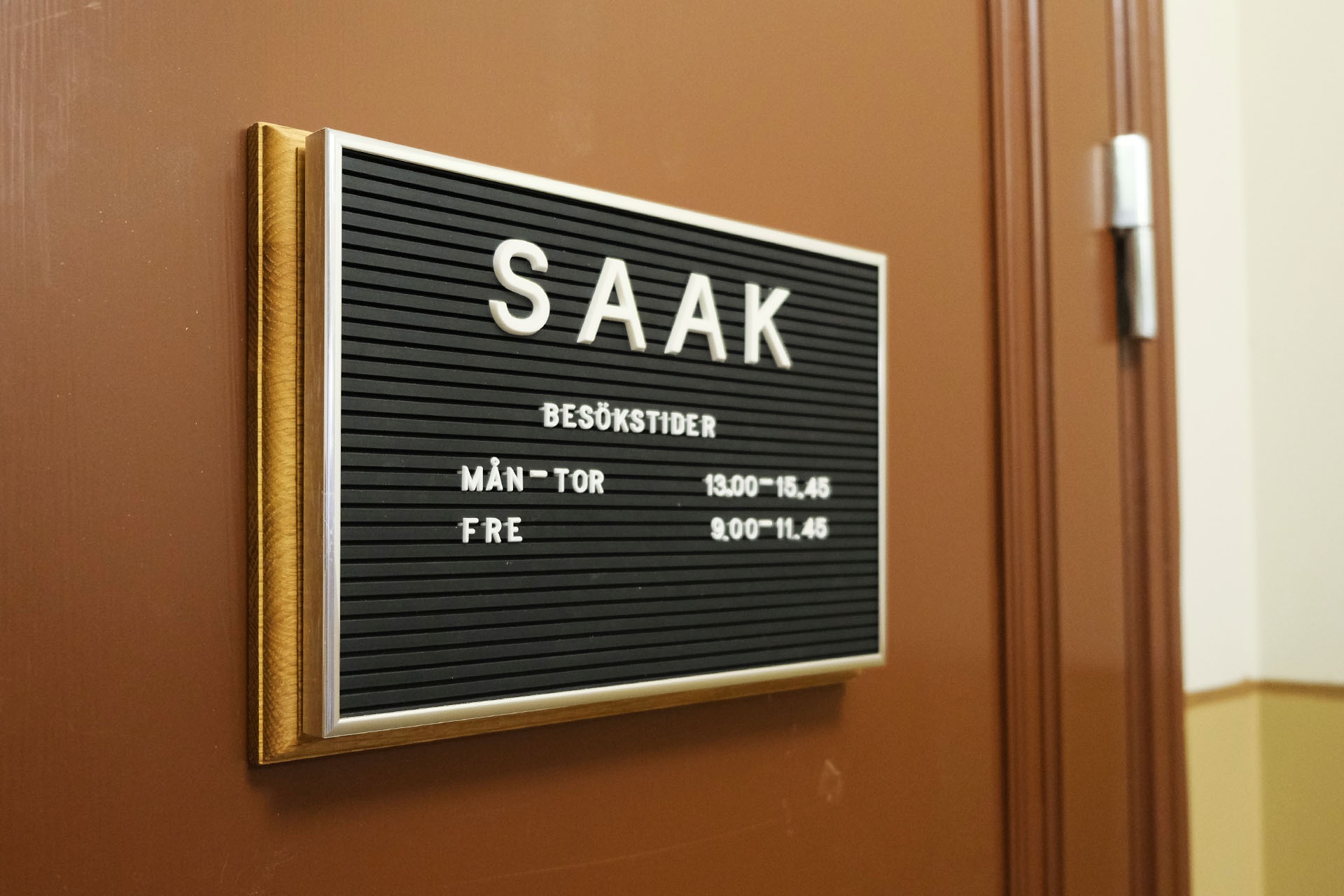 Skylt med vita bokstäver visar besökstider på SAAK, Sveriges Arbetares Arbetslöshetskassa
