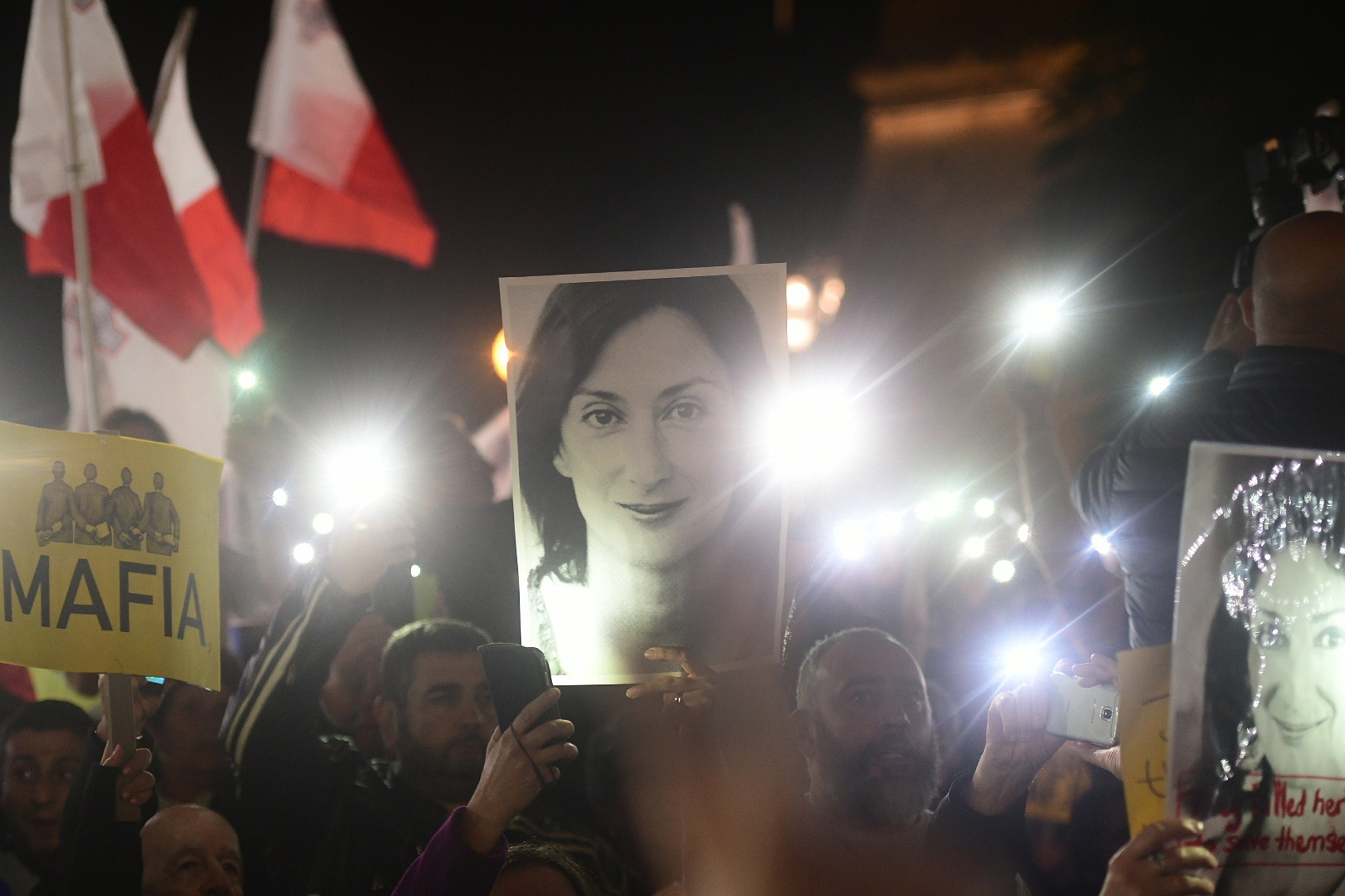 Demonstration i mörker, demonstranter håller upp lysande mobiltelefoner och en bild på den mördade journalisten Daphne Caruana Galizia.