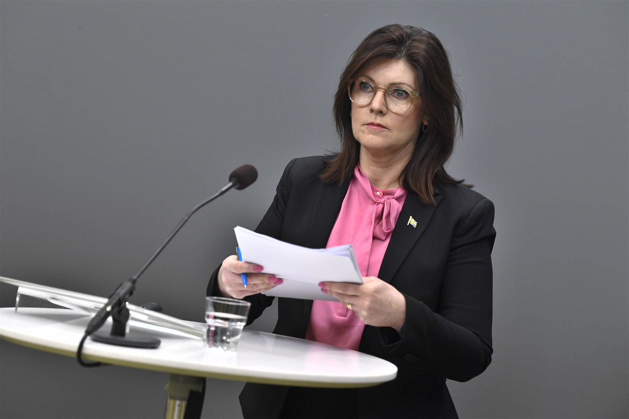 Eva Nordmark på pressträff om arbetslivskriminalitet, ståendes bakom ett högt vitt bord med en mikrofon.