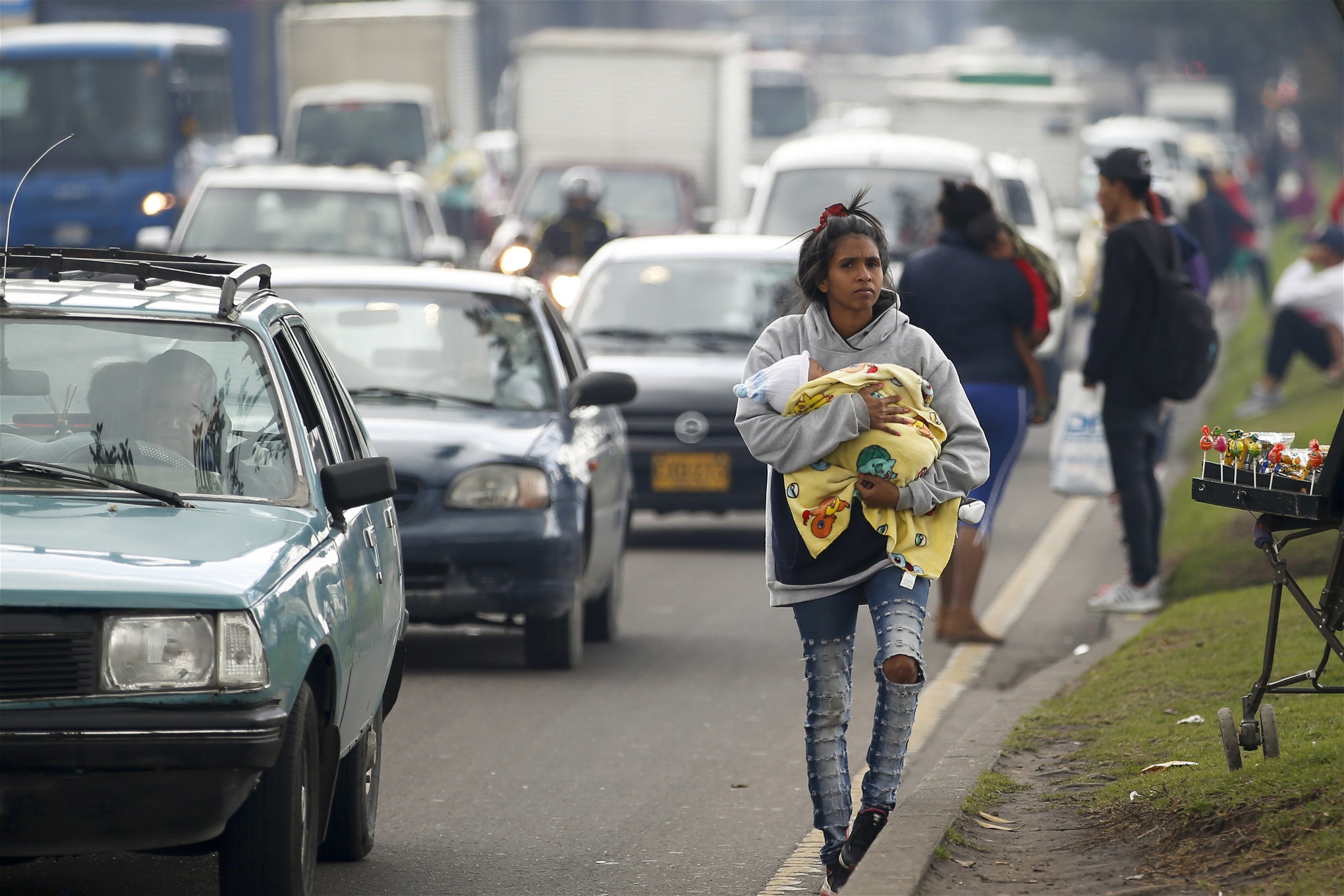 En venezolansk kvinna med ett spädbarn i famnen går längs en väg med bilar i Colombia.