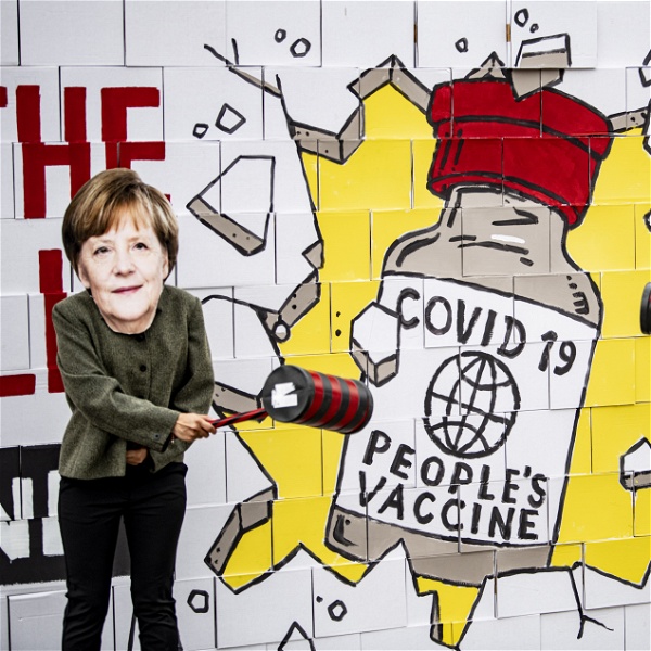 Aktivister med masker föreställande Angela Merkel och Joe Biden slår med släggor mot en väggmålning där en mur framför en bild av ett "folkets vaccin" krossas.