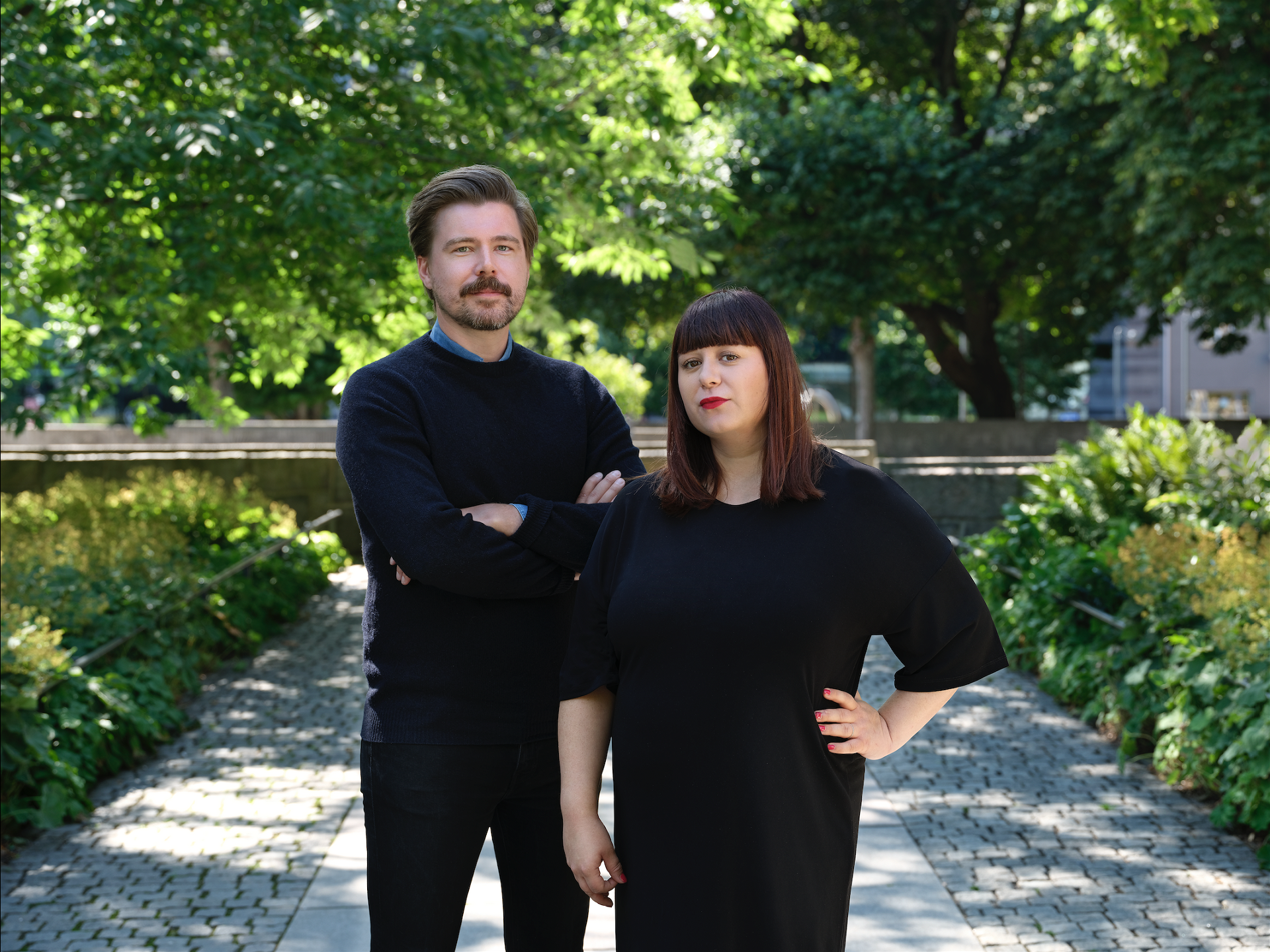 Karl Martinsson och Mira Hjort klädda i svart, utomhus med grönskande träd i bakgrunden.