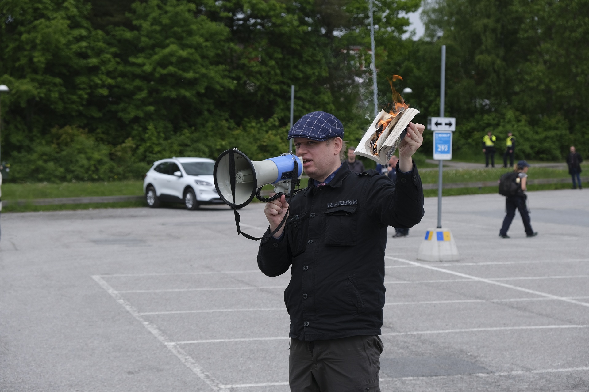 Ingen av de få åskådarna bryr sig nämnvärt när Paludan fjuttar eld på koranen på den öde parkeringsplatsen utanför Spånga IP. Foto: Johan Apel Röstlund