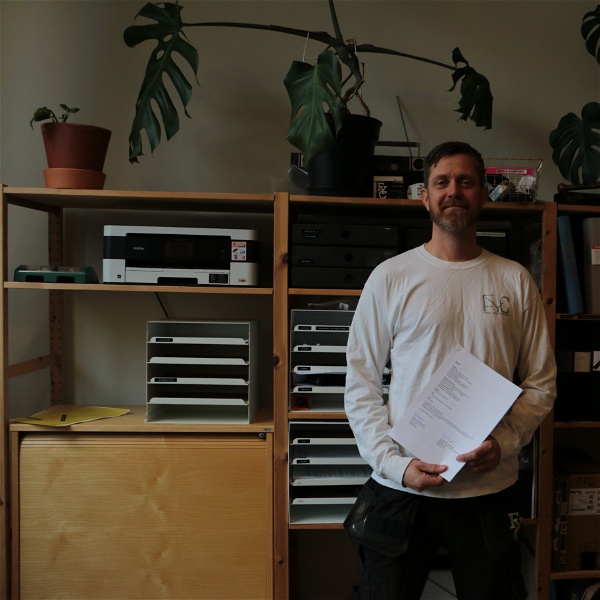Tobias Andersson står med ett kollektivavtal i handen framför en bokhylla